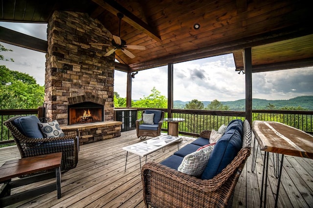 wooden terrace with a mountain view, an outdoor living space with a fireplace, and a ceiling fan