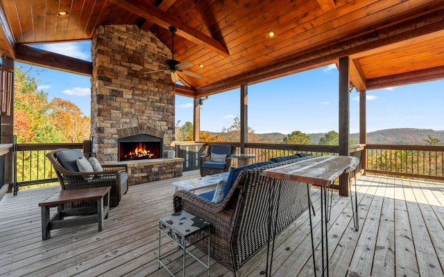 deck featuring an outdoor stone fireplace, a mountain view, and ceiling fan
