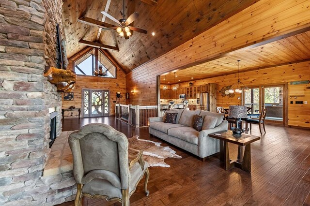 living area with a stone fireplace, wooden walls, hardwood / wood-style floors, high vaulted ceiling, and ceiling fan with notable chandelier