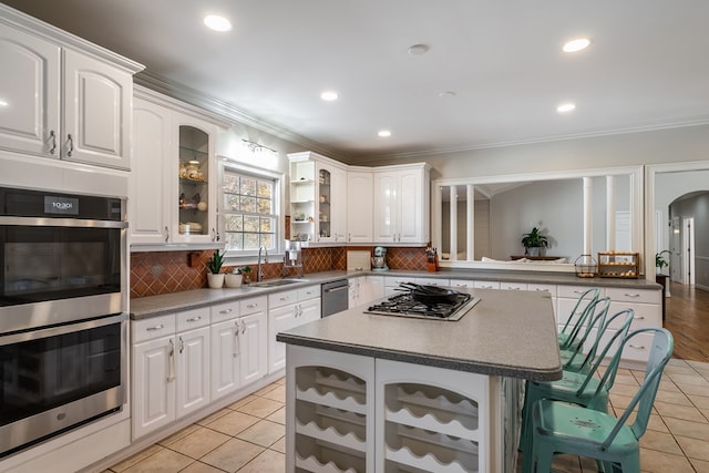 kitchen with a sink, stainless steel appliances, light tile patterned floors, glass insert cabinets, and a kitchen bar