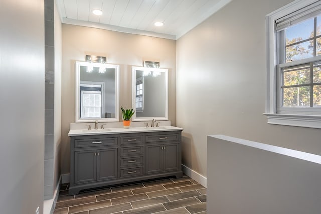 bathroom featuring a sink, double vanity, baseboards, wood finish floors, and recessed lighting