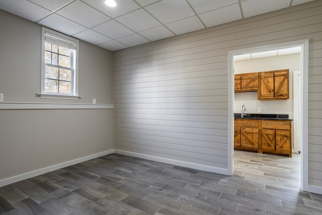 unfurnished room featuring a sink, wood tiled floor, wood walls, baseboards, and a drop ceiling