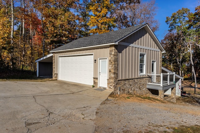 exterior space featuring a detached garage, a shingled roof, concrete driveway, and stone siding