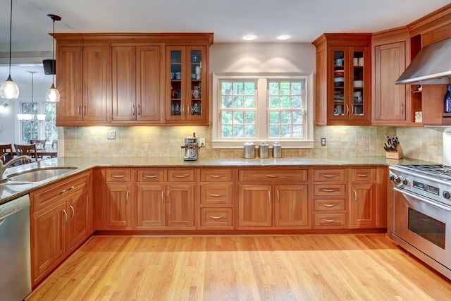 kitchen featuring appliances with stainless steel finishes, brown cabinetry, a sink, and wall chimney exhaust hood