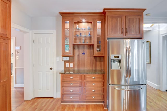 kitchen with brown cabinetry, glass insert cabinets, dark stone countertops, stainless steel refrigerator with ice dispenser, and light wood-style flooring