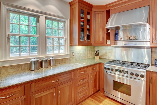 kitchen featuring light stone counters, brown cabinetry, glass insert cabinets, and high end stove