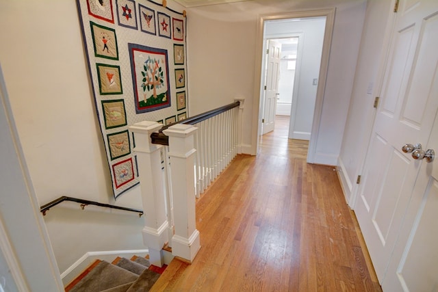 corridor featuring baseboards, an upstairs landing, and light wood-type flooring