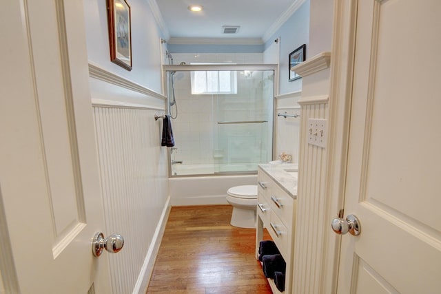 full bath featuring crown molding, toilet, wood finished floors, visible vents, and bath / shower combo with glass door