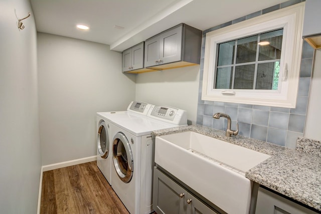 laundry room featuring dark wood finished floors, cabinet space, a sink, baseboards, and separate washer and dryer