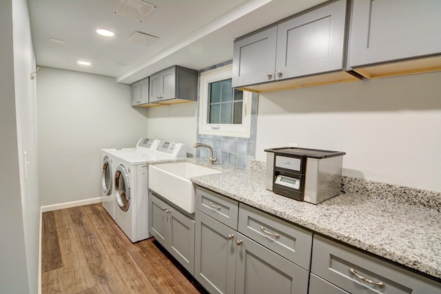 laundry area with cabinet space, a sink, baseboards, wood finished floors, and washing machine and dryer