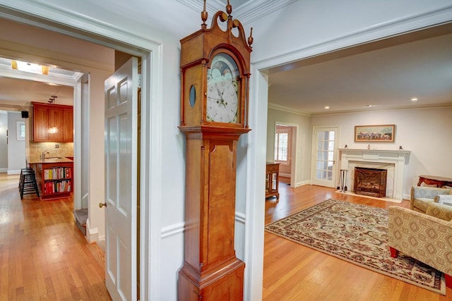 hallway with crown molding, a sink, light wood-style flooring, and baseboards