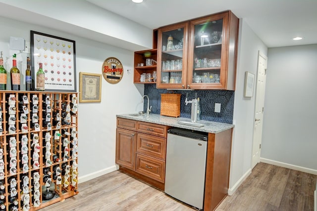 bar featuring backsplash, wet bar, fridge, a sink, and light wood-style flooring