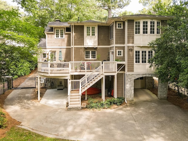 back of house featuring a wooden deck, a chimney, stairs, a gate, and concrete driveway