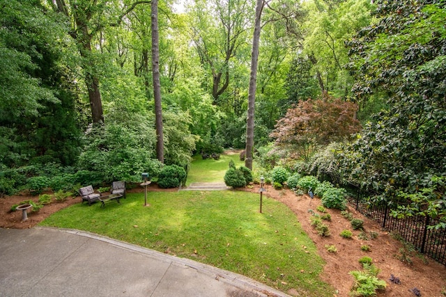 view of community with a lawn, a forest view, and fence