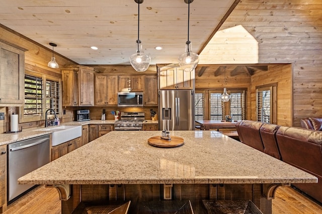 kitchen with appliances with stainless steel finishes, sink, wood walls, and pendant lighting