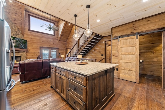 kitchen featuring wood walls, wood-type flooring, hanging light fixtures, stainless steel refrigerator, and a center island