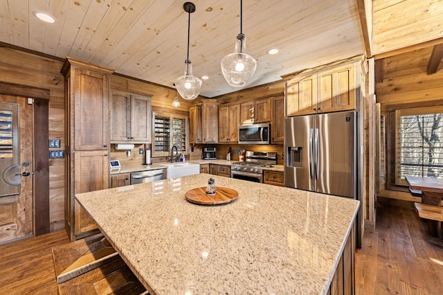 kitchen with wood walls, pendant lighting, a center island, sink, and stainless steel appliances