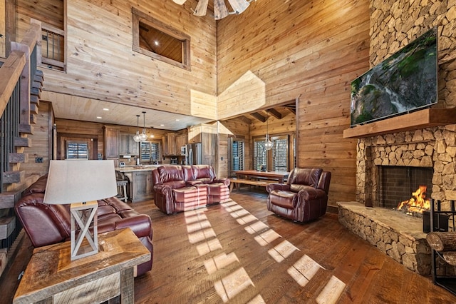 living room featuring dark hardwood / wood-style flooring, a fireplace, a towering ceiling, rustic walls, and ceiling fan with notable chandelier