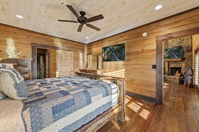 bedroom with wood ceiling, wooden walls, a stone fireplace, ceiling fan, and dark hardwood / wood-style flooring