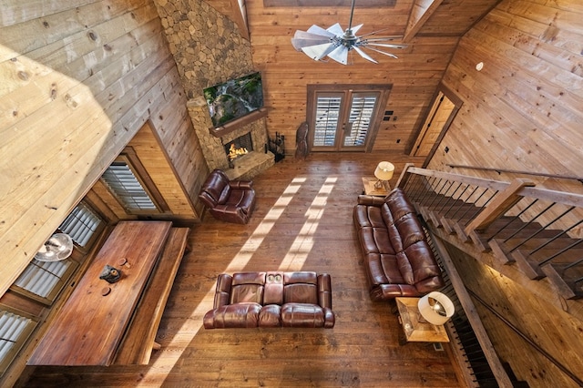 unfurnished living room featuring wooden walls, ceiling fan, a high ceiling, and a stone fireplace