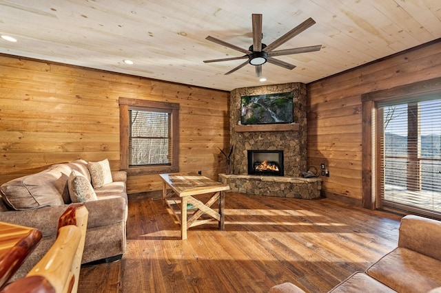 living room with hardwood / wood-style flooring, ceiling fan, a stone fireplace, and wood ceiling