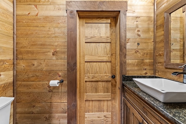 bathroom featuring toilet, vanity, and wood walls