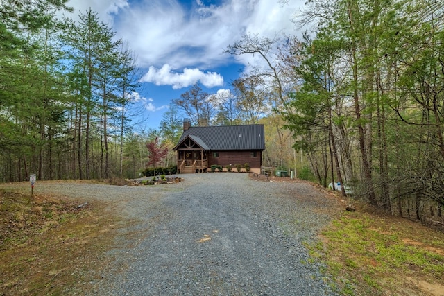 view of front of house featuring gravel driveway, a chimney, a forest view, and metal roof