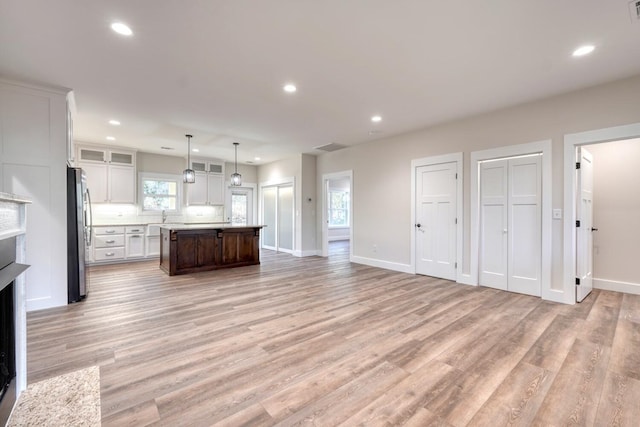 kitchen with light hardwood / wood-style flooring, decorative light fixtures, a kitchen island, white cabinetry, and stainless steel refrigerator