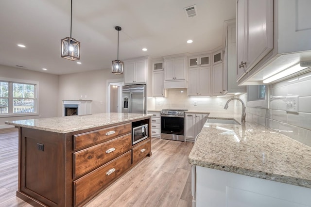 kitchen with stainless steel appliances, pendant lighting, a kitchen island, white cabinets, and sink