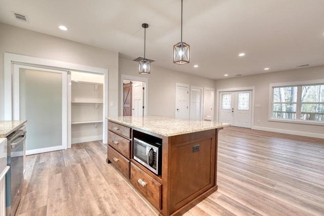 kitchen with stainless steel appliances, decorative light fixtures, a center island, and light stone countertops