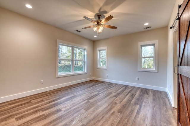 unfurnished room featuring ceiling fan, a healthy amount of sunlight, light hardwood / wood-style floors, and a barn door