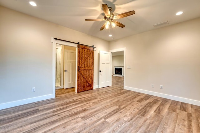 unfurnished bedroom featuring ceiling fan, a barn door, and light hardwood / wood-style flooring