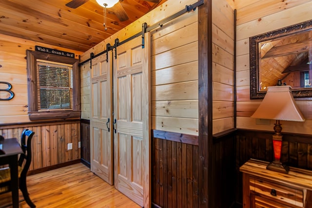 interior space featuring wood ceiling, wood walls, a barn door, and light wood-type flooring