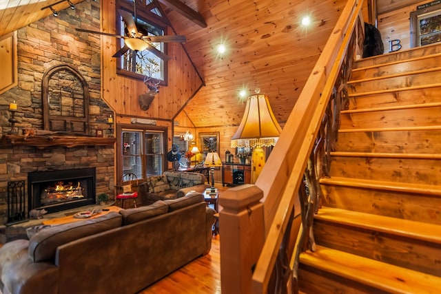 living room featuring wood ceiling, wooden walls, a stone fireplace, high vaulted ceiling, and beam ceiling