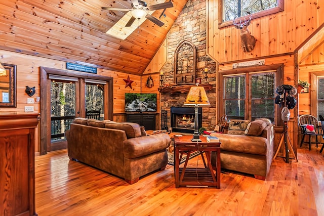 living room featuring wood walls, wood-type flooring, a stone fireplace, high vaulted ceiling, and wooden ceiling