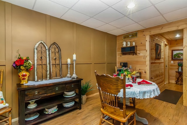 dining room with a paneled ceiling, light wood-type flooring, and wood walls