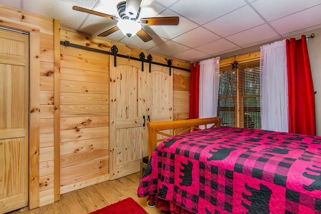 bedroom with ceiling fan, a drop ceiling, wooden walls, and hardwood / wood-style floors