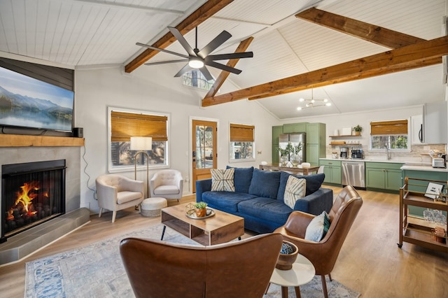 living area featuring vaulted ceiling with beams, light wood-style flooring, a fireplace, and a ceiling fan