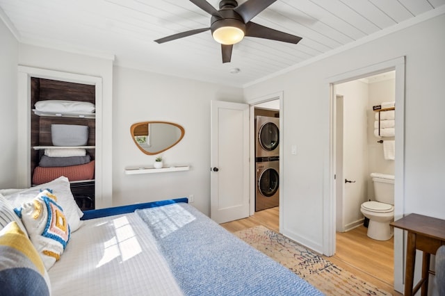 bedroom with ceiling fan, connected bathroom, ornamental molding, stacked washing maching and dryer, and light wood finished floors