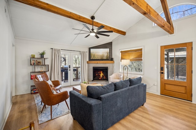 living area with a ceiling fan, lofted ceiling with beams, a lit fireplace, french doors, and light wood-type flooring