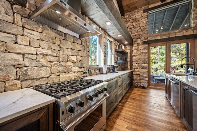 kitchen featuring sink, wall chimney range hood, light stone counters, appliances with stainless steel finishes, and hardwood / wood-style flooring