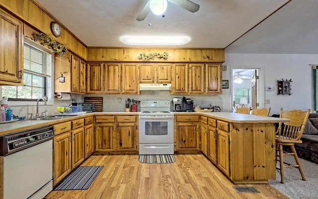 kitchen featuring kitchen peninsula, a breakfast bar, white appliances, sink, and light hardwood / wood-style floors