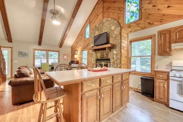 kitchen with white stove, a kitchen bar, a fireplace, light hardwood / wood-style flooring, and vaulted ceiling with beams