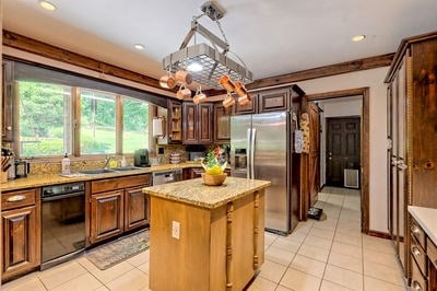 kitchen featuring a center island, sink, stainless steel refrigerator with ice dispenser, light tile patterned flooring, and light stone counters