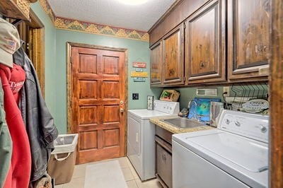 clothes washing area featuring cabinets, light tile patterned floors, a textured ceiling, and separate washer and dryer