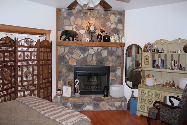 living room with ceiling fan, a stone fireplace, and hardwood / wood-style floors