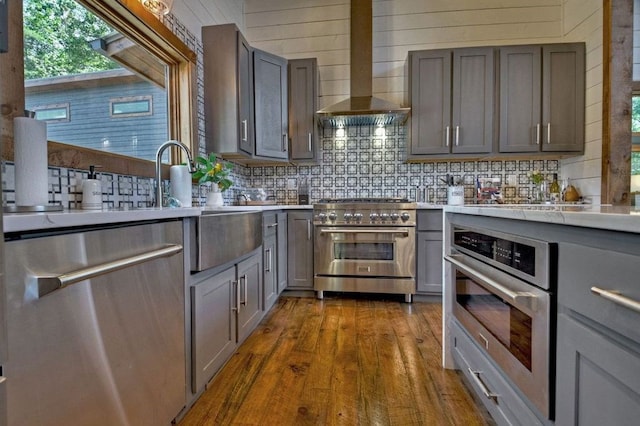 kitchen featuring gray cabinetry, stainless steel appliances, dark hardwood / wood-style flooring, and wall chimney range hood