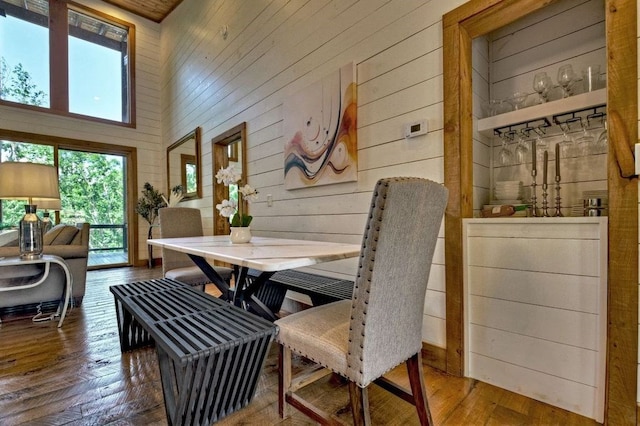 dining space featuring a towering ceiling, hardwood / wood-style floors, and wood walls