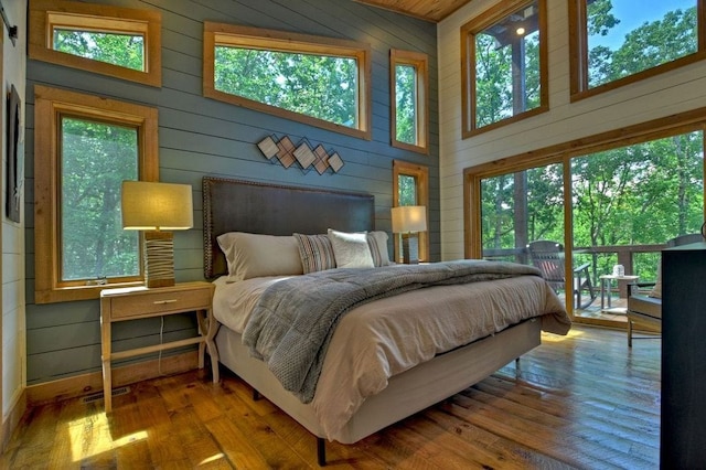 bedroom with a high ceiling, wood-type flooring, access to outside, and wooden walls