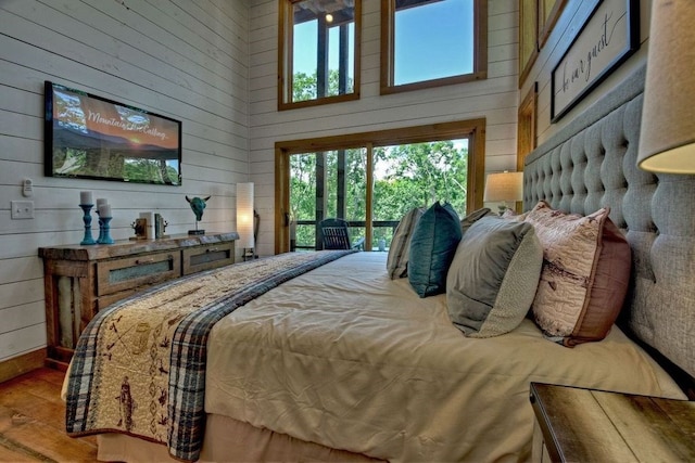 bedroom featuring hardwood / wood-style flooring, access to outside, a high ceiling, and wood walls